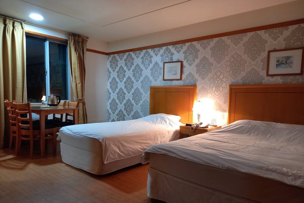 A hotel room with two beds, a desk with a chair, a lamp, and a window with curtains.