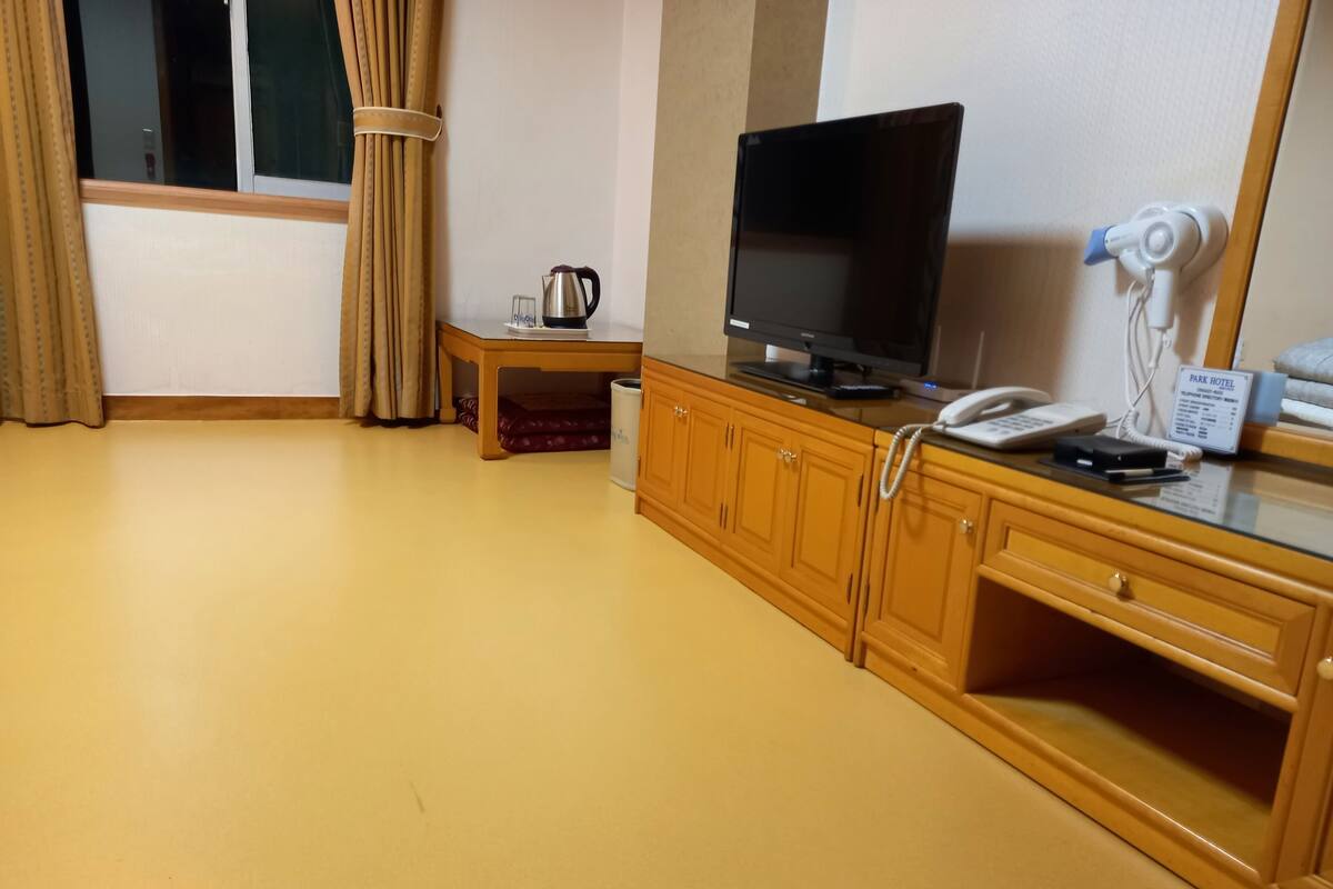 A hotel room with a wooden cabinet, a television, a telephone, and a small table with a kettle.