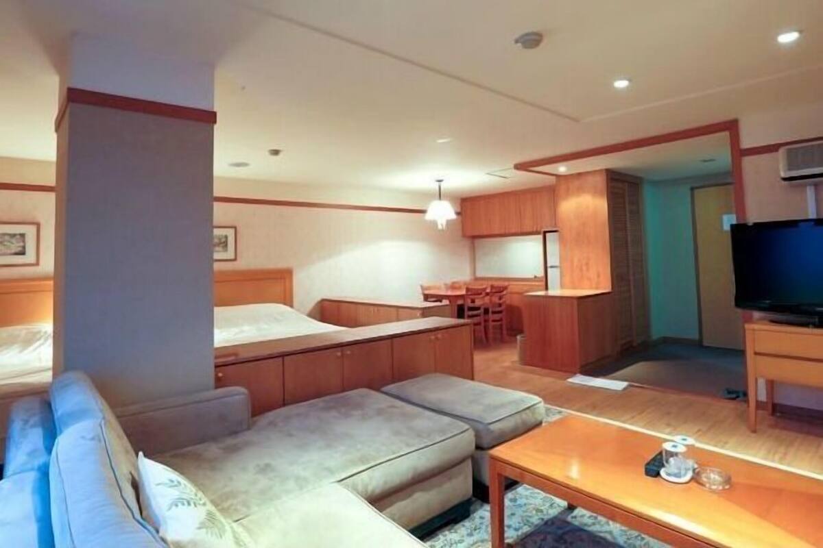A hotel room with a sofa, a small dining table, a kitchenette, and a television.