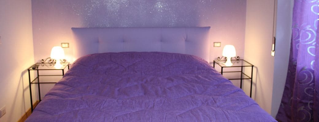 Ein Bett mit Kopfteil, zwei Nachttische jeweils mit Lampe, und eine Wand mit Sternenprojektion.