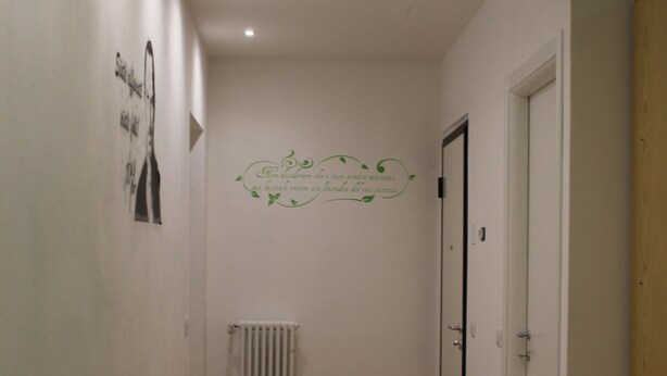A hallway with wooden flooring, a radiator, a door, and a wall with a green decorative sticker. - Affittacamere Pavia (Pavia)