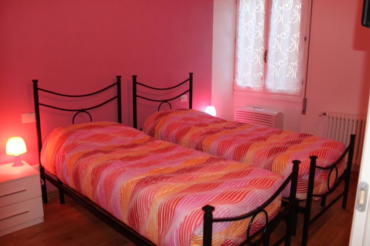 A twin bed with a striped bedspread in a room with pink walls and a window with patterned curtains.