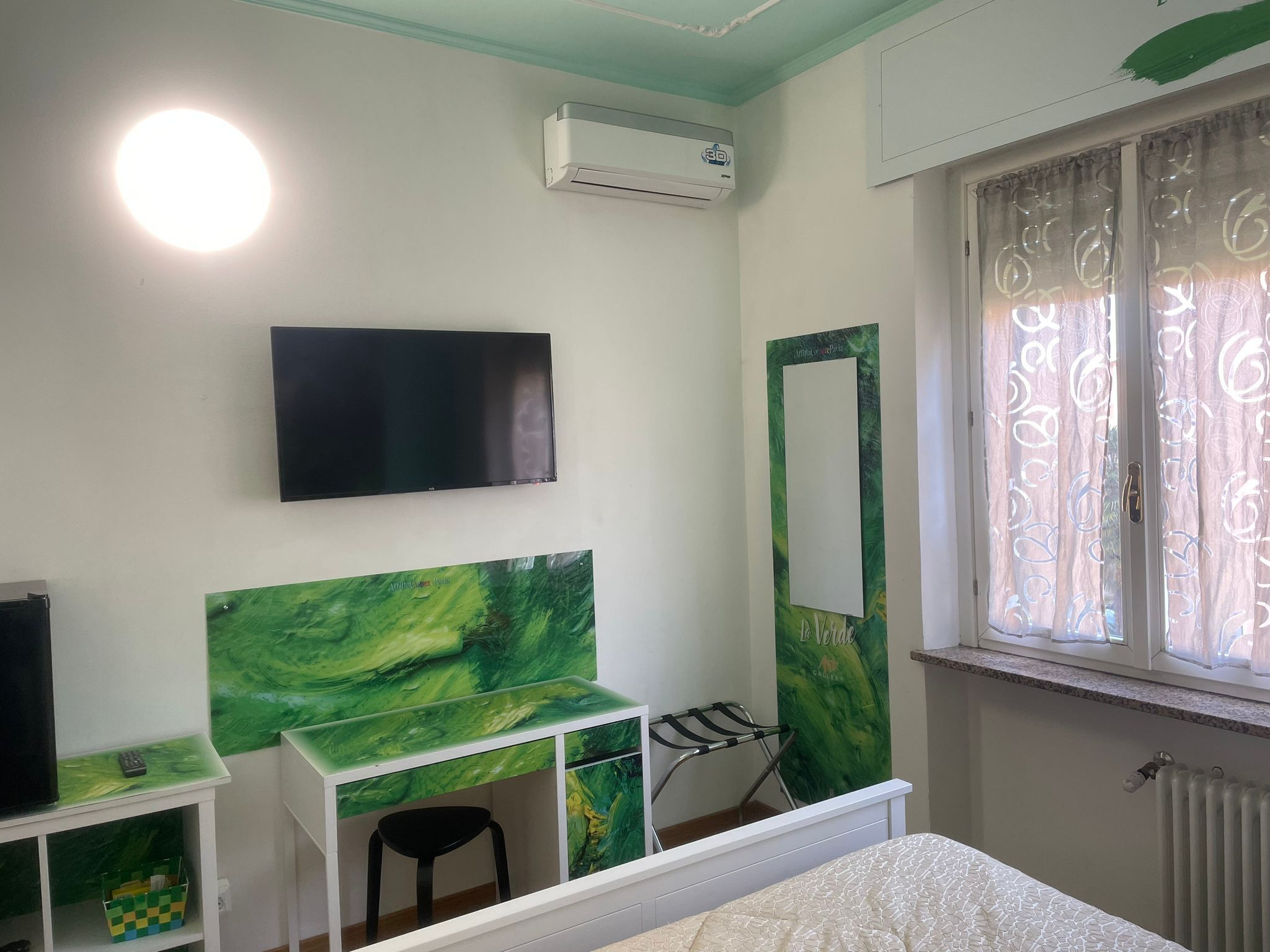 Une chambre à coucher comprenant un lit, une télévision, un bureau avec une chaise, un miroir et une fenêtre avec des rideaux.