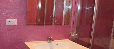 A bathroom with a white sink, red cabinets, a large mirror, and a shower area.