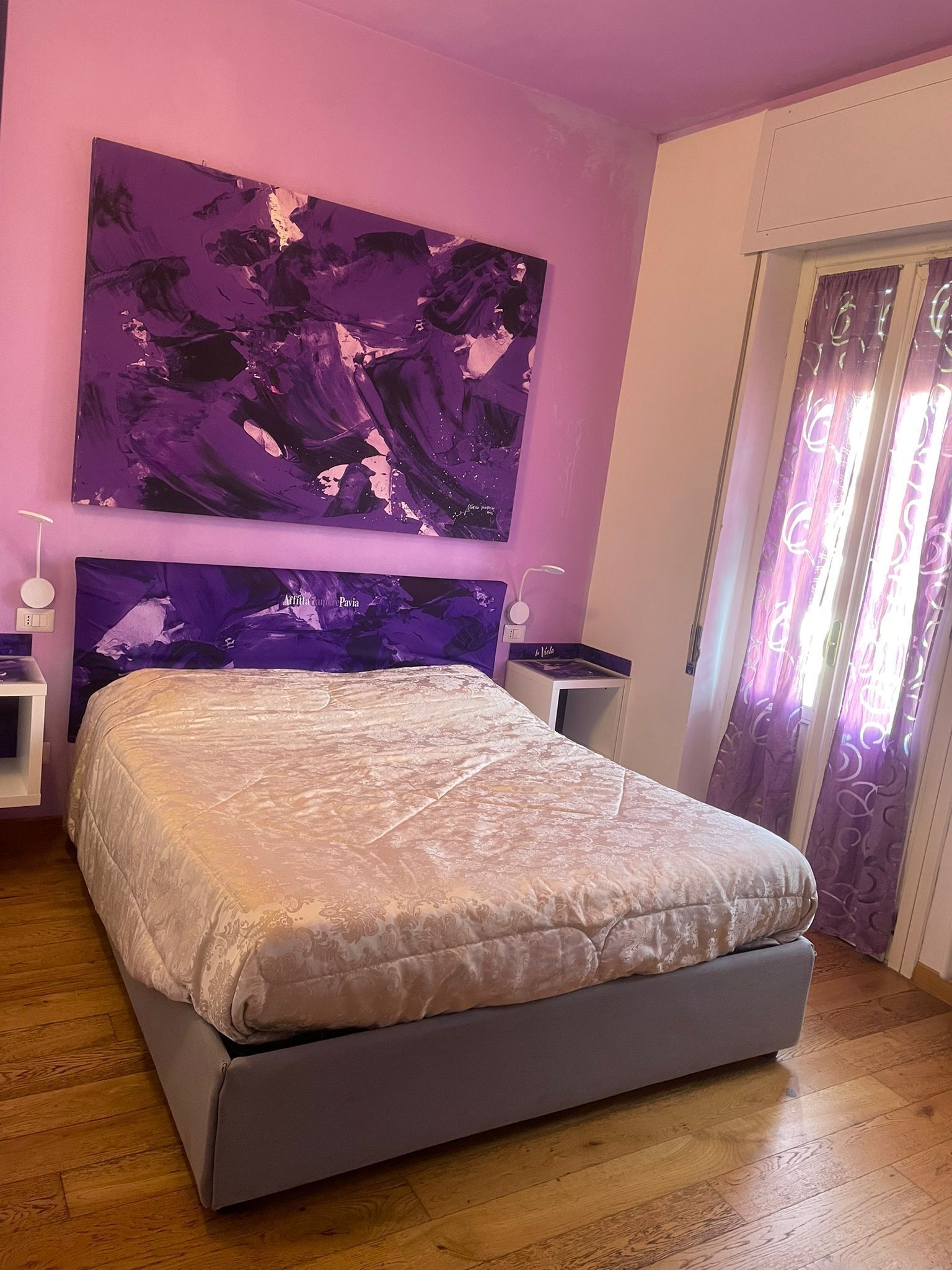 Une chambre à coucher avec un lit, une table de chevet, une lampe et un grand tableau abstrait accroché au mur.