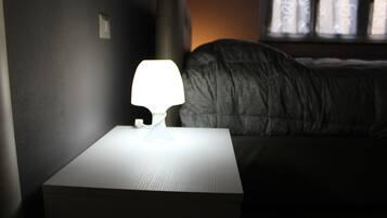 A bedside table with a lamp, a bed with a dark blanket, and a window with curtains.