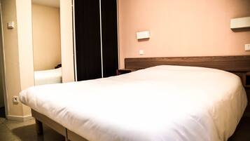 A hotel room with a large bed, a wooden headboard, a bedside table, and a wall-mounted light.