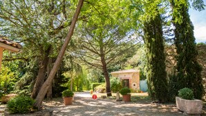 Un jardín con un sendero de grava, macetas de piedra y un pequeño edificio con tejado de tejas.
