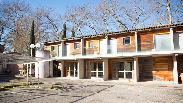 Un edificio de dos pisos con fachada de madera, ventanas amplias y un espacio exterior cubierto.
