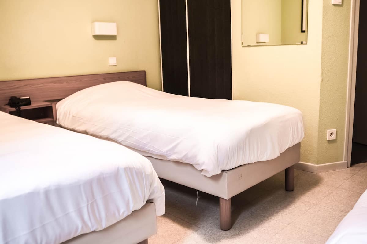 Hotellihuone, jossa on kaksi erillistä sänkyä, puinen pääty, yöpöytä, yölamppu, peili ja ovi.