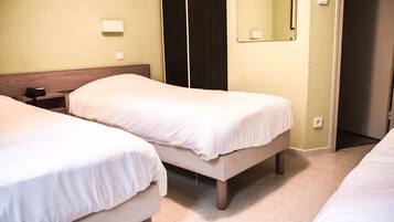 Une chambre d’hôtel avec deux lits simples, une tête de lit en bois, une table de chevet, une lampe de chevet, un miroir et une porte.