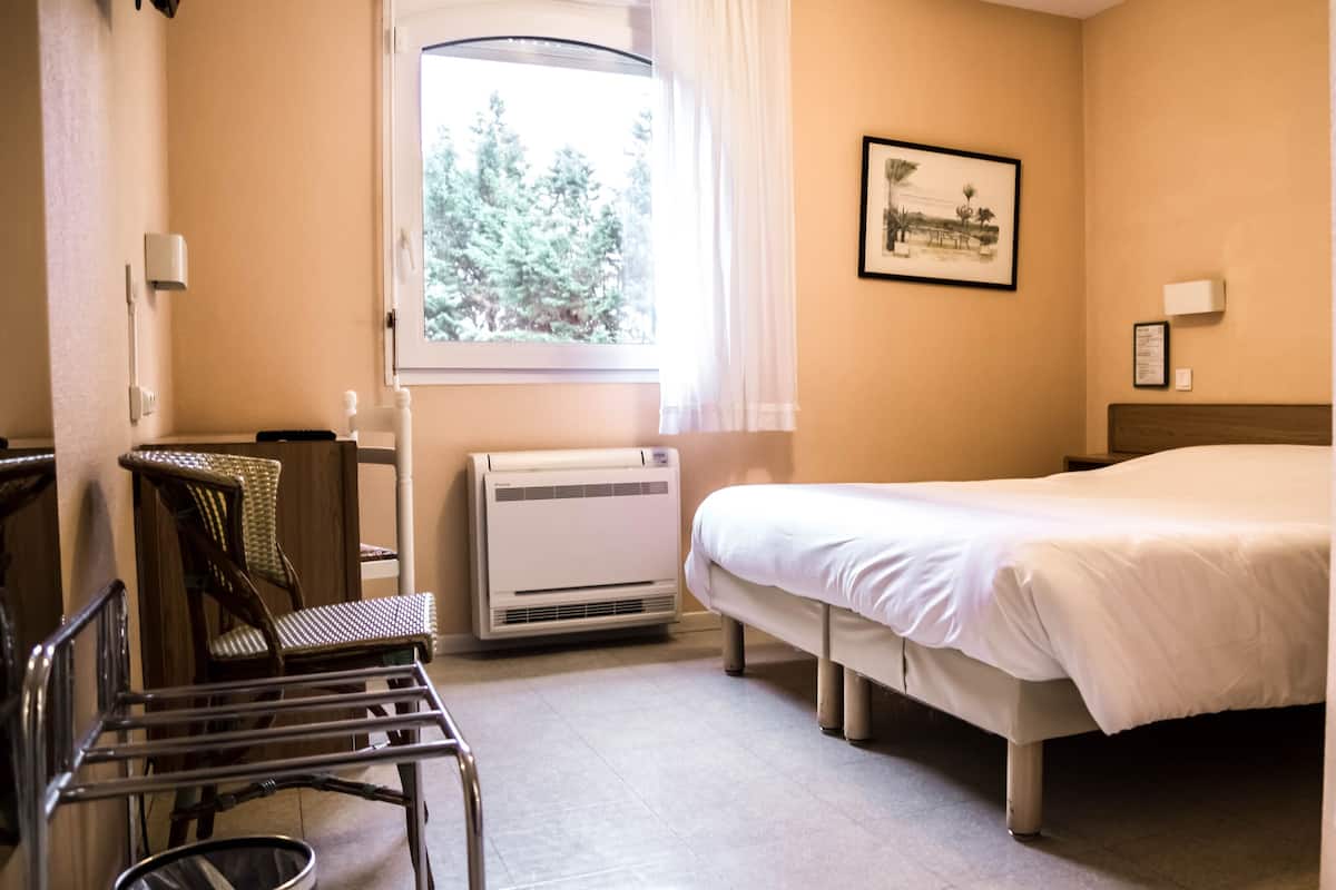 Hotellihuone, jossa on sänky, tuoli, työpöytä ja ikkuna, josta on näkymä puita kohti.