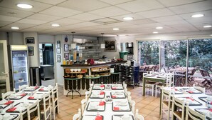 Restaurante con mesas dispuestas para comer, zona de bar y vista a árboles a través de amplios ventanales.