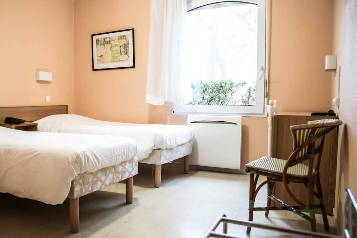 Hotellihuone, jossa on kaksi sänkyä, työpöytä, tuoli ja ikkuna, josta on näkymä puita kohti.