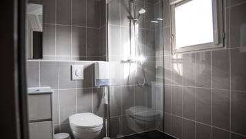 A modern bathroom with a glass-enclosed shower, a toilet, and a hand dryer.