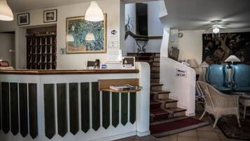 A hotel lobby with a reception desk, a staircase, a blue sofa, and a painting on the wall.