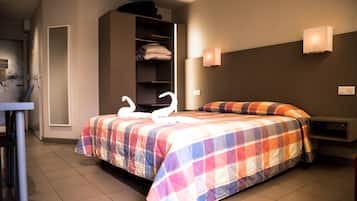 A hotel room with a bed, a wardrobe, a nightstand, and a wall-mounted light fixture.