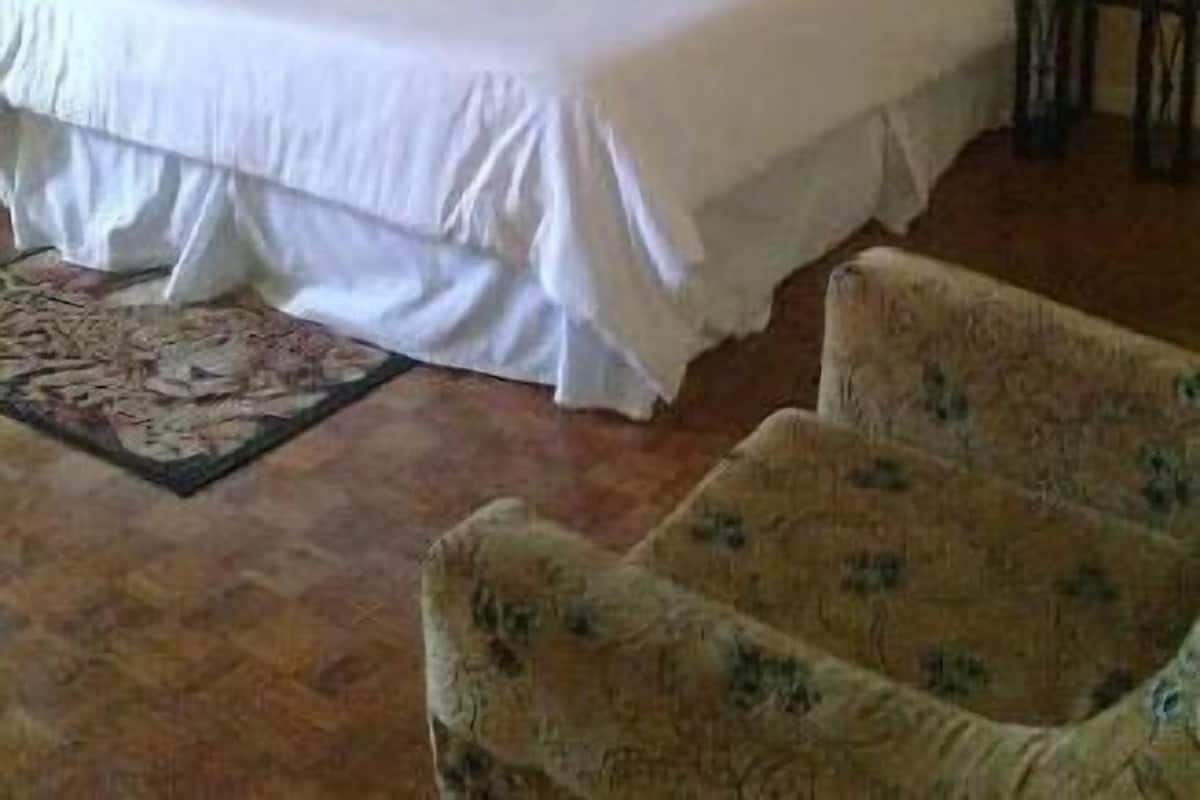 A hotel room with a bed, a chair, a small table, and a painting on the wall.