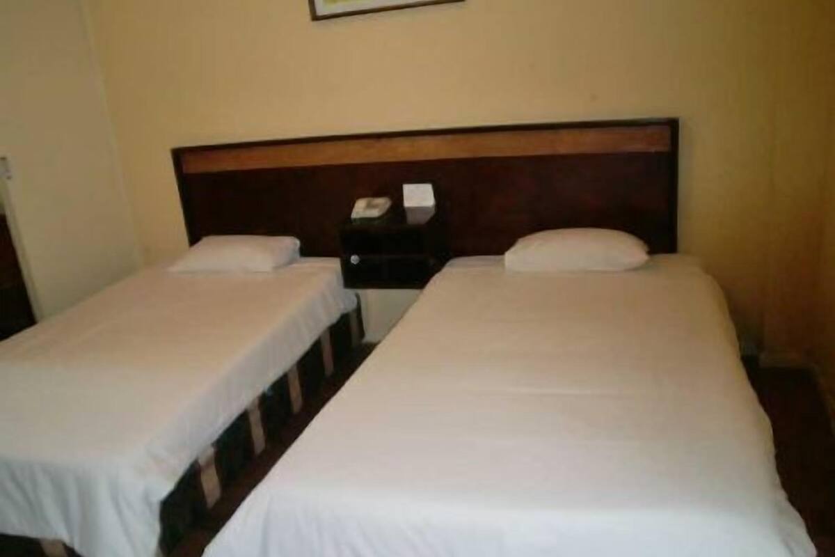Two single beds with wooden headboards, white bedding, and a small bedside table with a lamp.