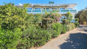 Un hotel de fachada blanca y detalles en verde, rodeado de abundante vegetación y un cielo azul despejado.