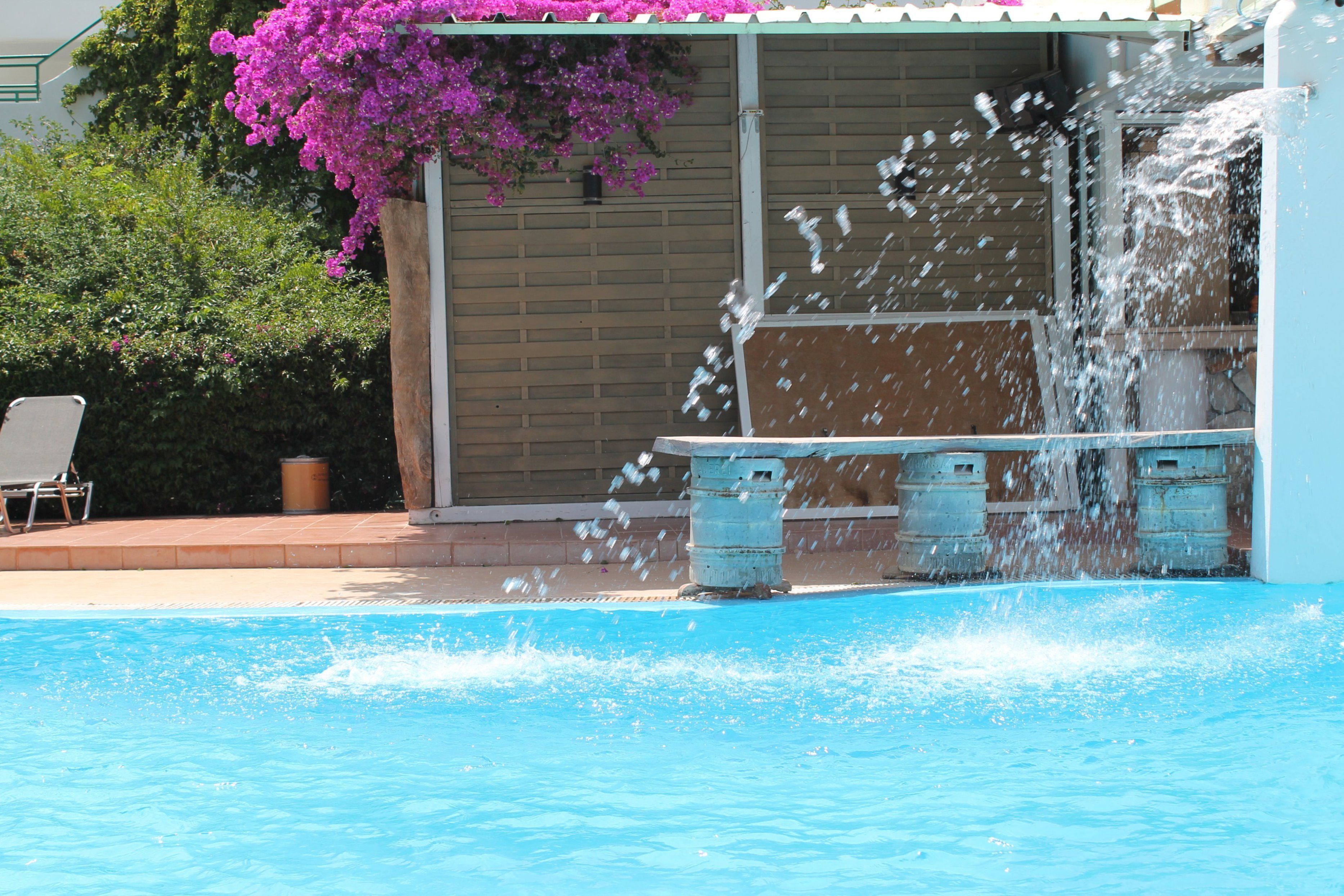 Piscina com jatos de água, uma cadeira e um vaso com flores roxas.