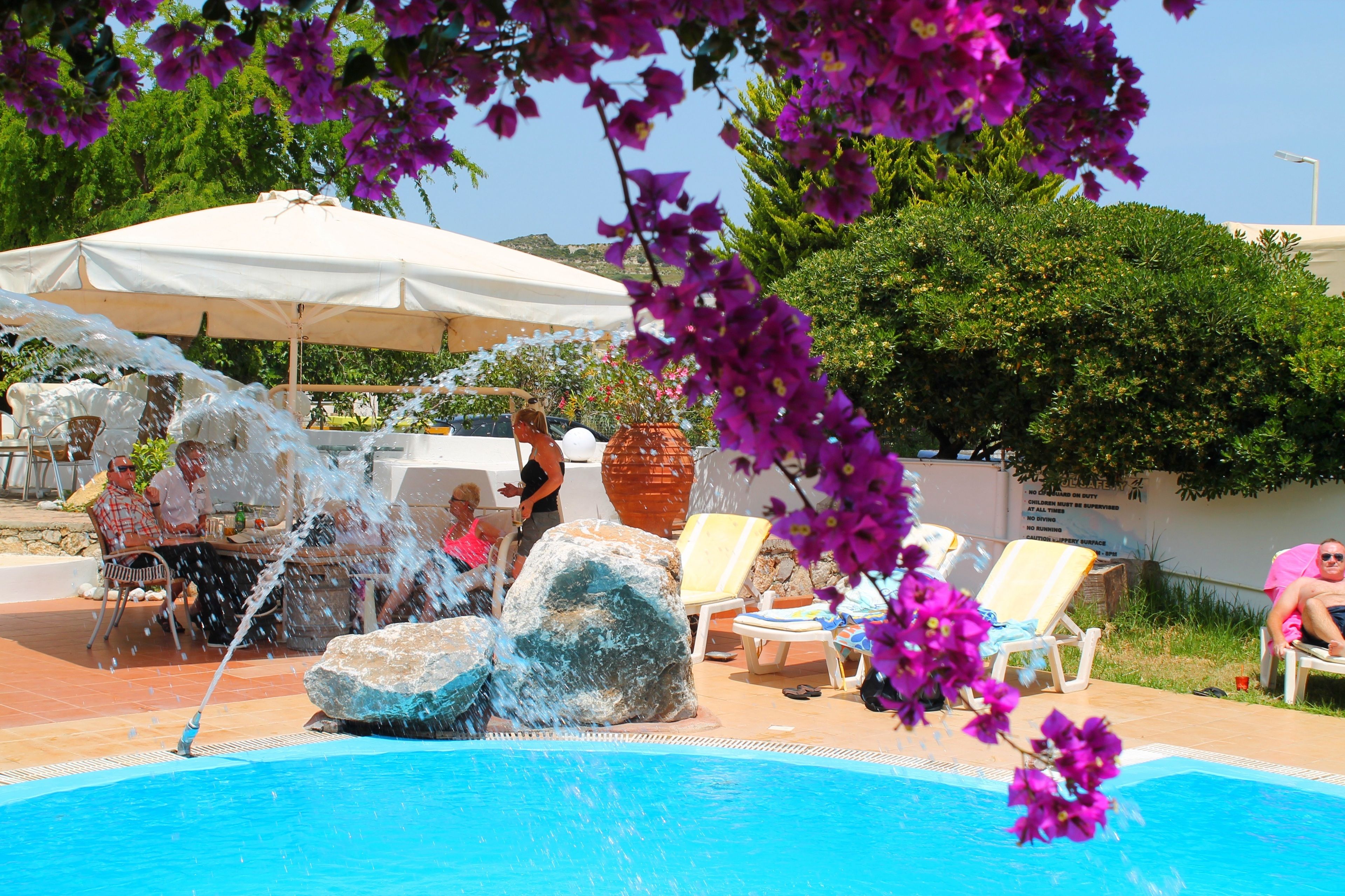 A pool area with a water feature, lounge chairs, and umbrellas.