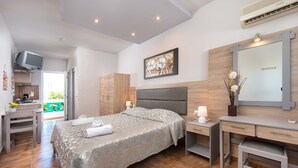 Un dormitorio con cama, mesitas de noche, escritorio, silla, televisor y baño visible a través de una puerta abierta.