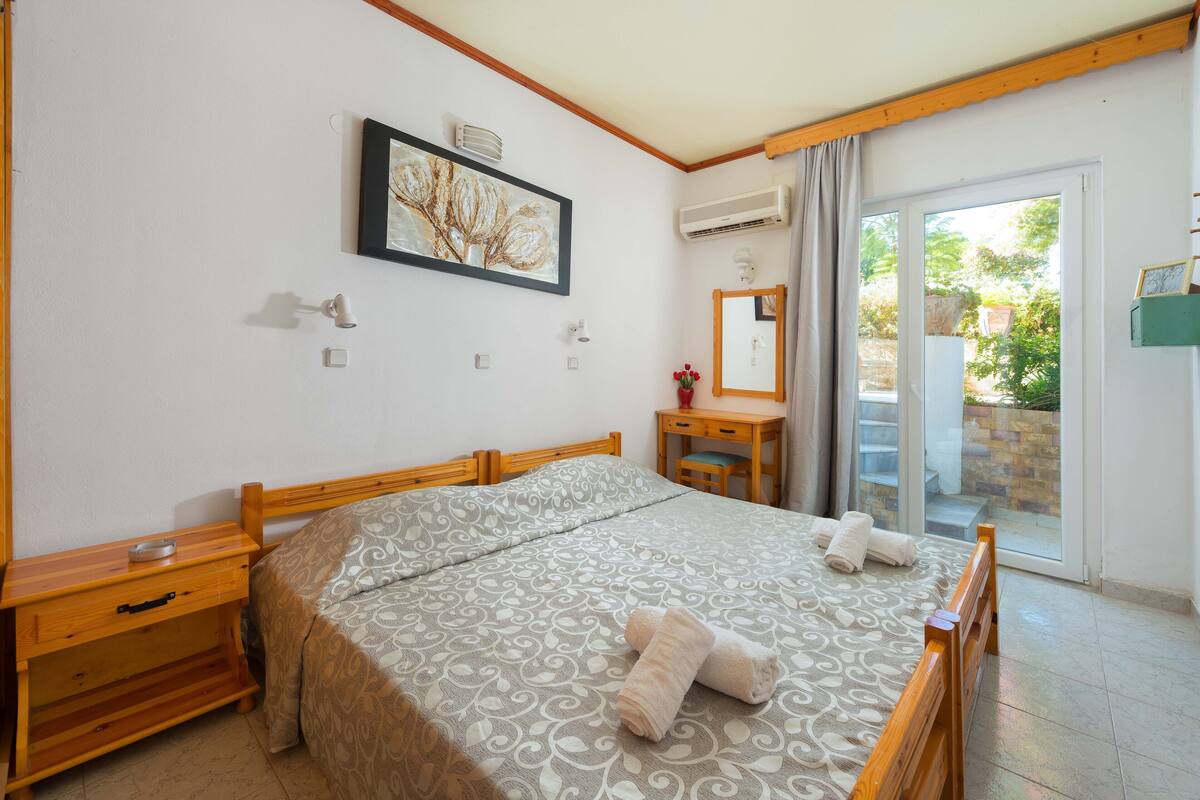 A bedroom with a bed, wooden nightstands, a dresser, a mirror, and a sliding glass door to a balcony.