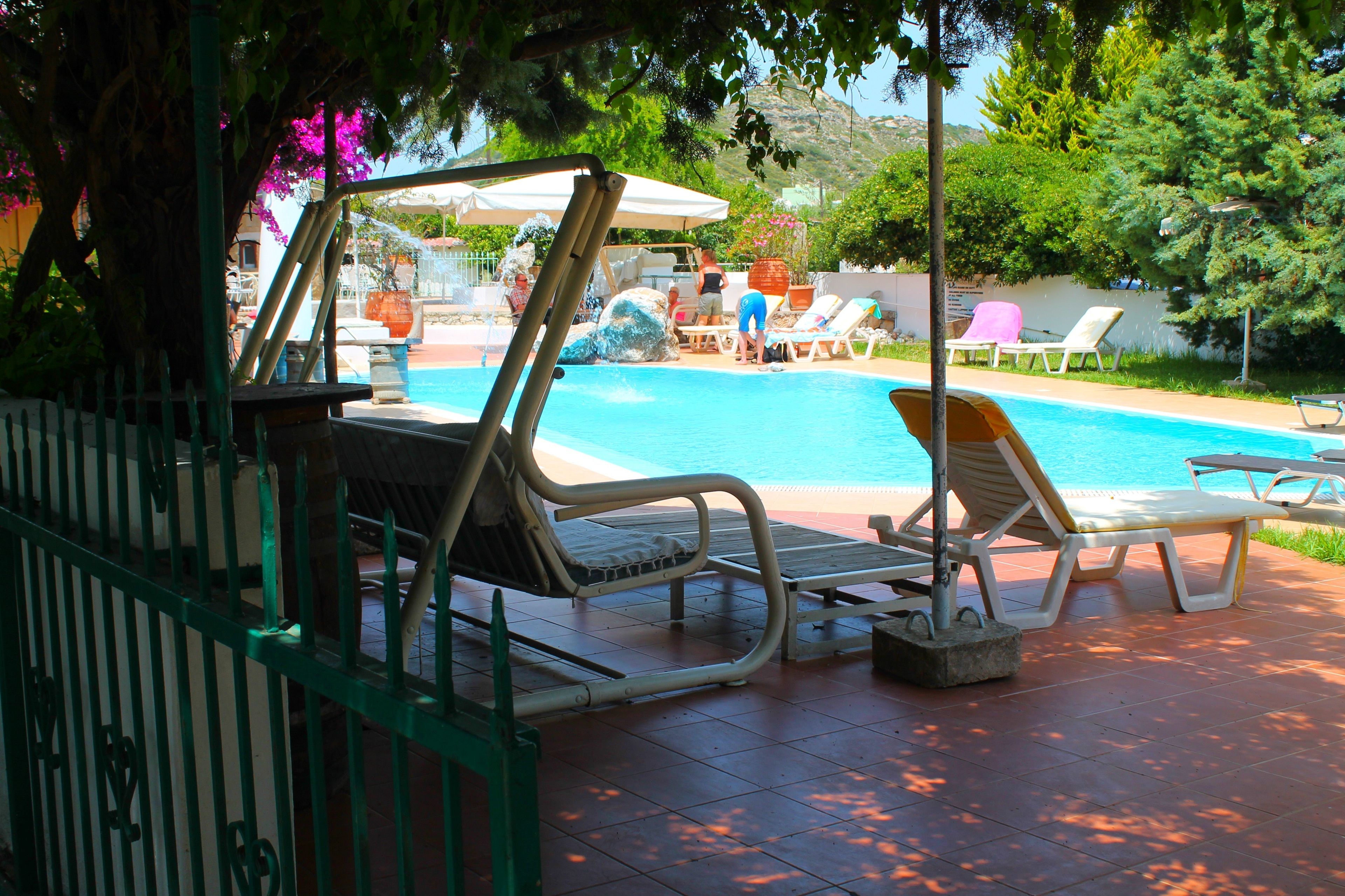 A poolside area with lounge chairs, a covered seating area, and a view of the pool.