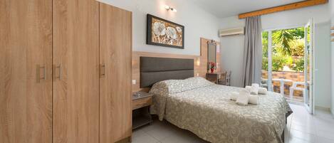 A bedroom with a large wardrobe, a bed with a patterned bedspread, a nightstand, and a window with a view of greenery.