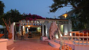 Un hotel moderno con zona de bar, asientos exteriores y una gran formación rocosa como elemento central.