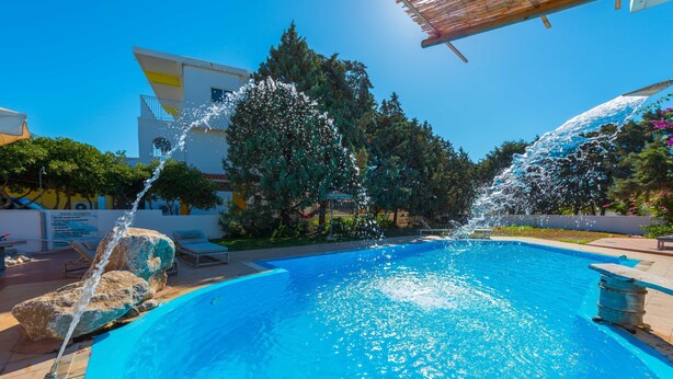 Una piscina con chorros de agua, rodeada de sillones de descanso y un edificio.