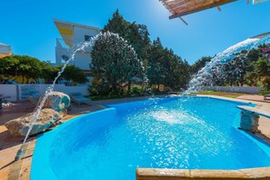 A swimming pool with water jets, surrounded by lounge chairs and a building. - Melody Studios (Rhodes)
