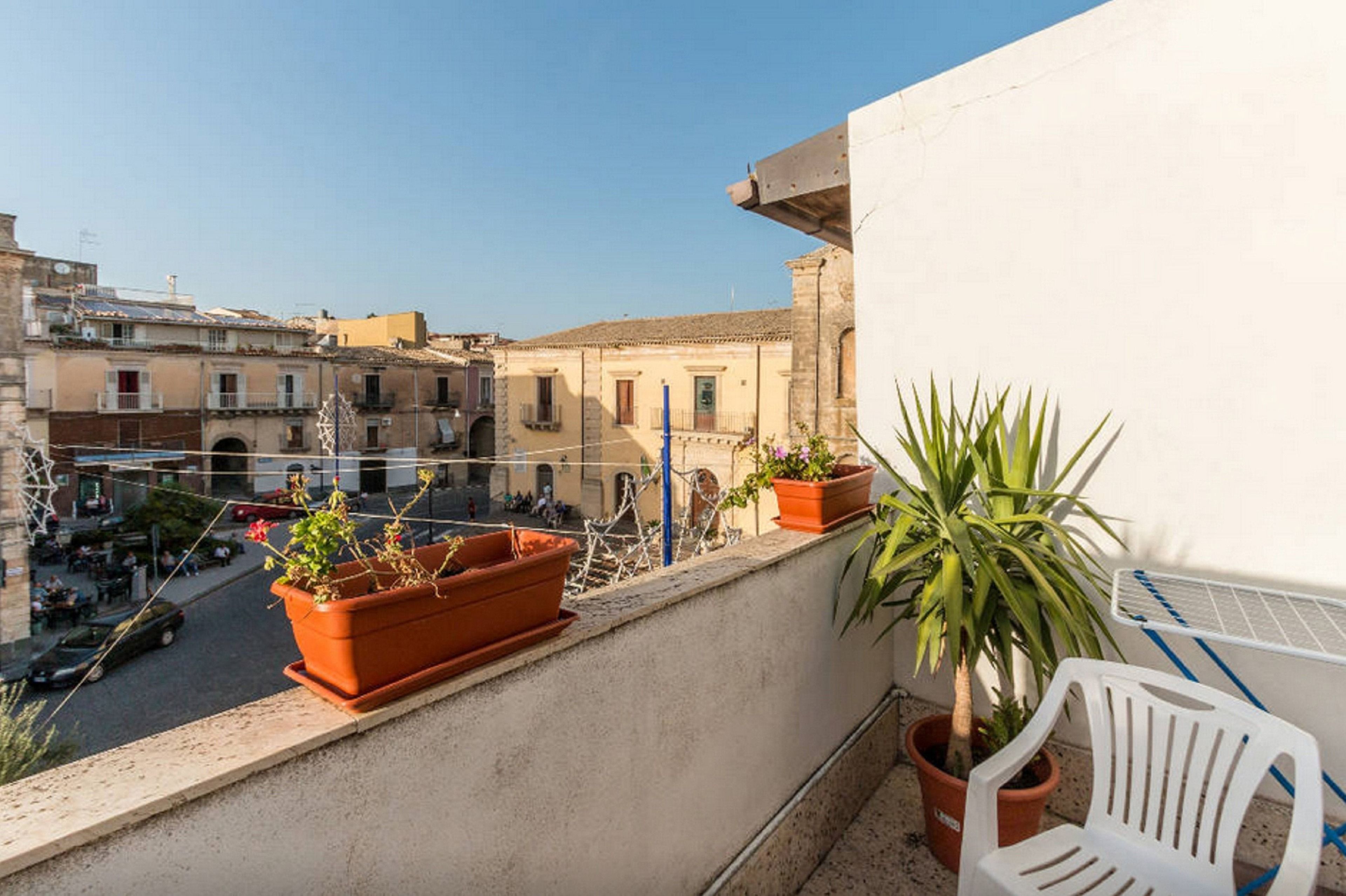 Een balkon met terracotta potten, een plant in pot en een witte stoel.