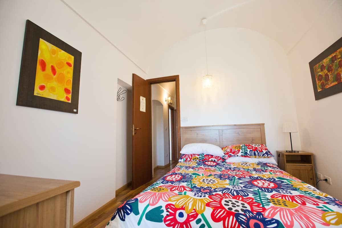 Un dormitorio con una colcha floral de colores, un cabecero de madera, una mesita de noche y una mesita auxiliar.