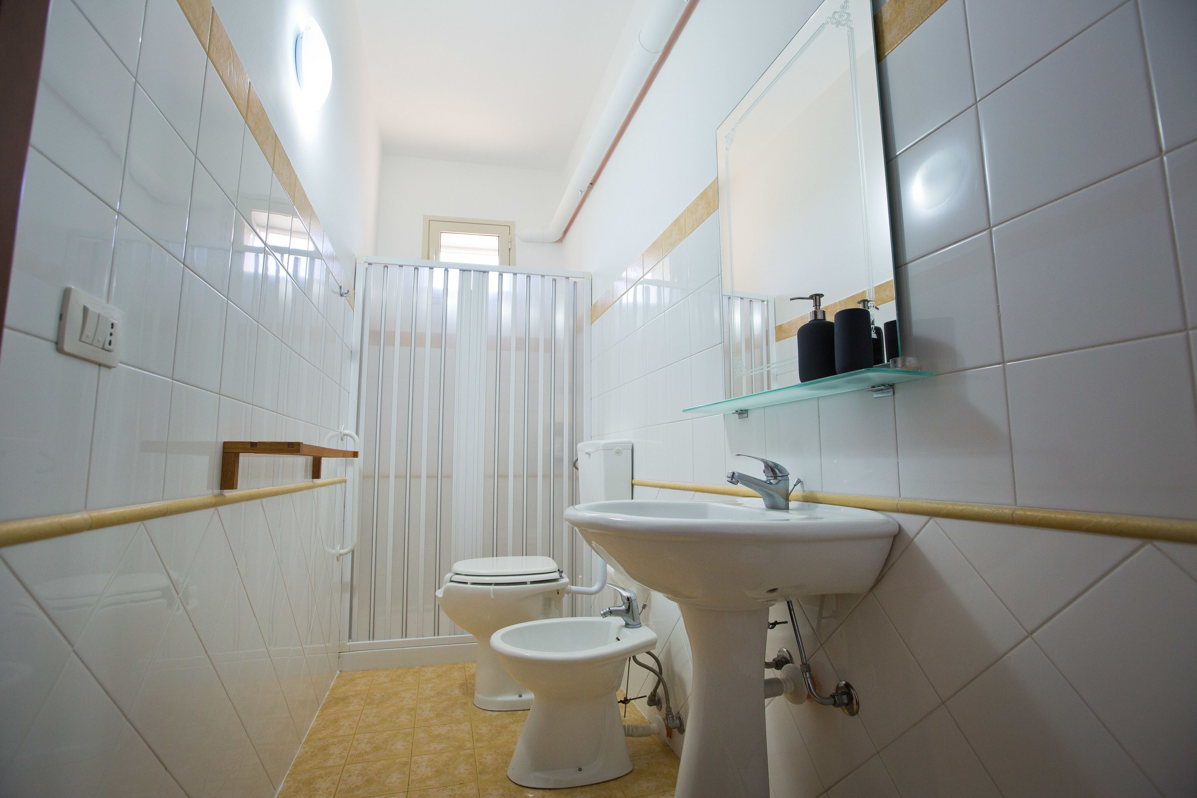 Un baño con azulejos blancos, un lavamanos pedestal, un inodoro y un bidé.