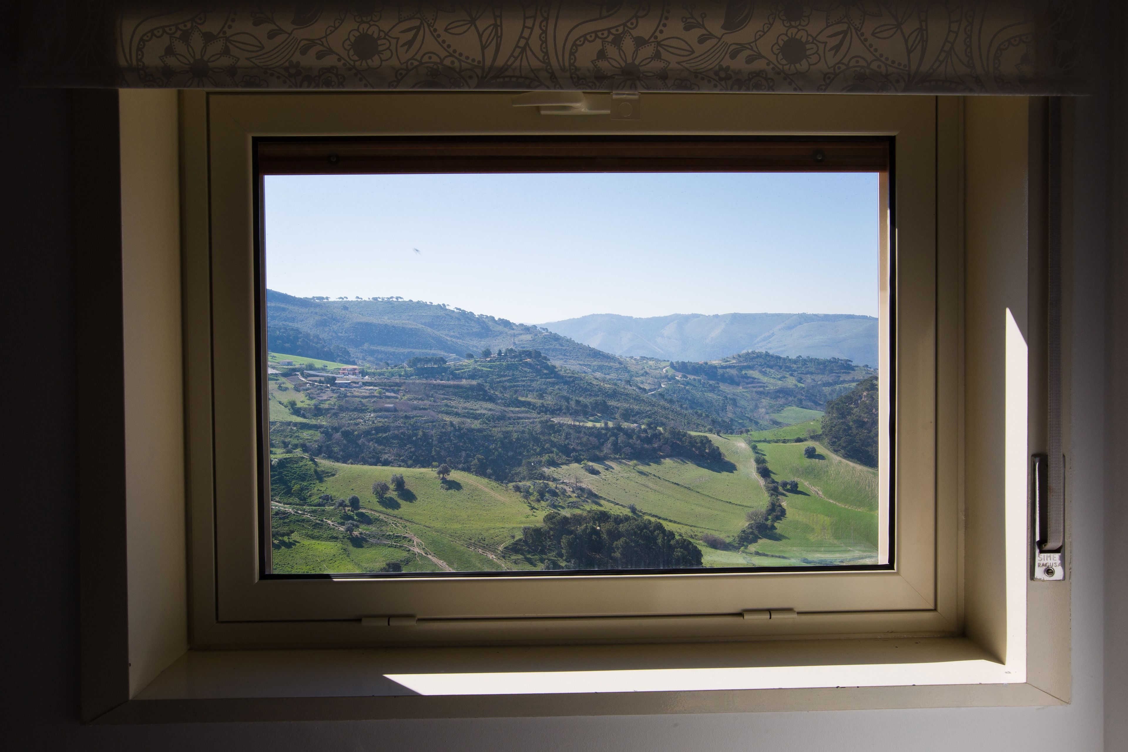 Una ventana con vistas a un valle verde y colinas.