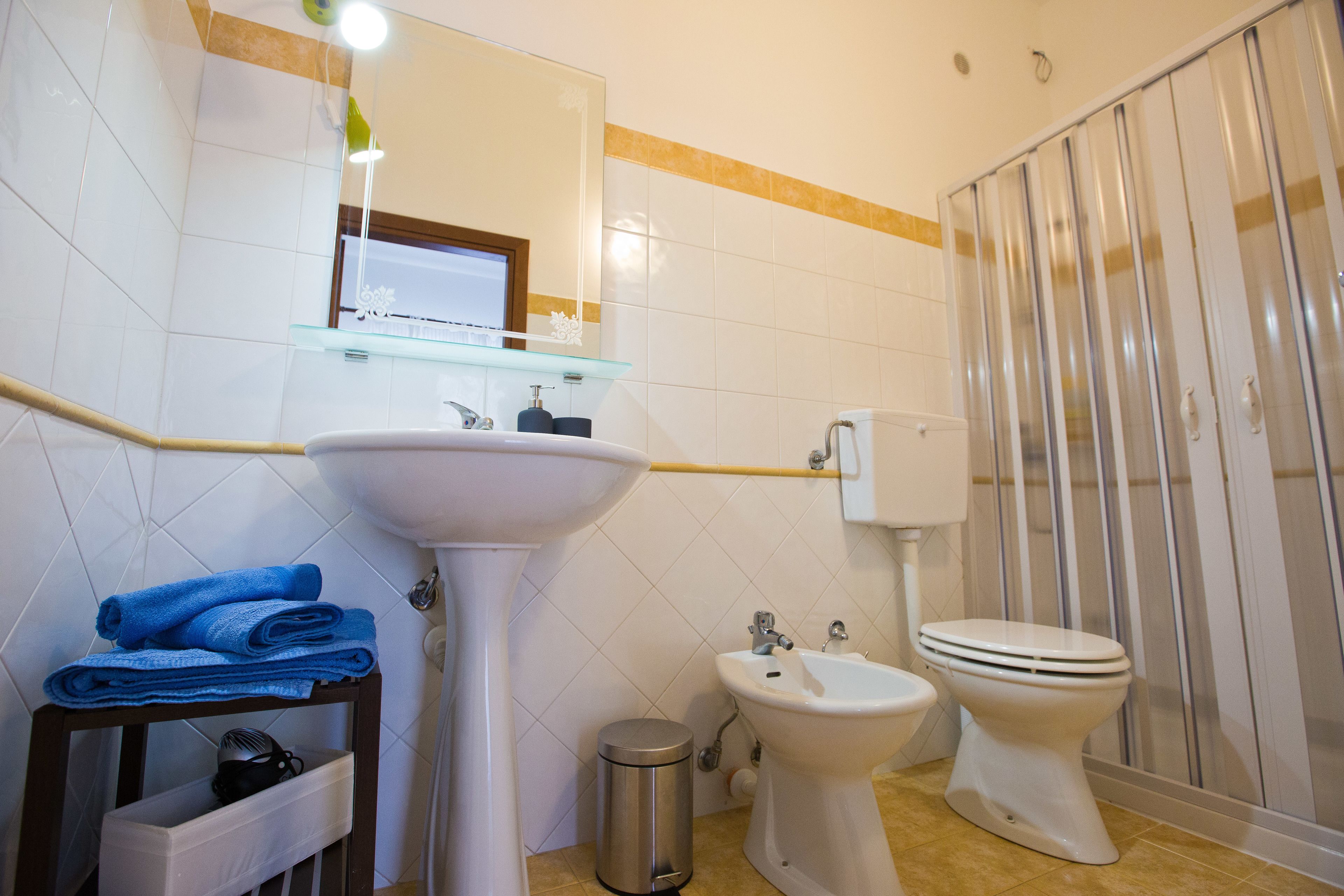 A bathroom with a sink, bidet, toilet, and a glass shelf with towels.