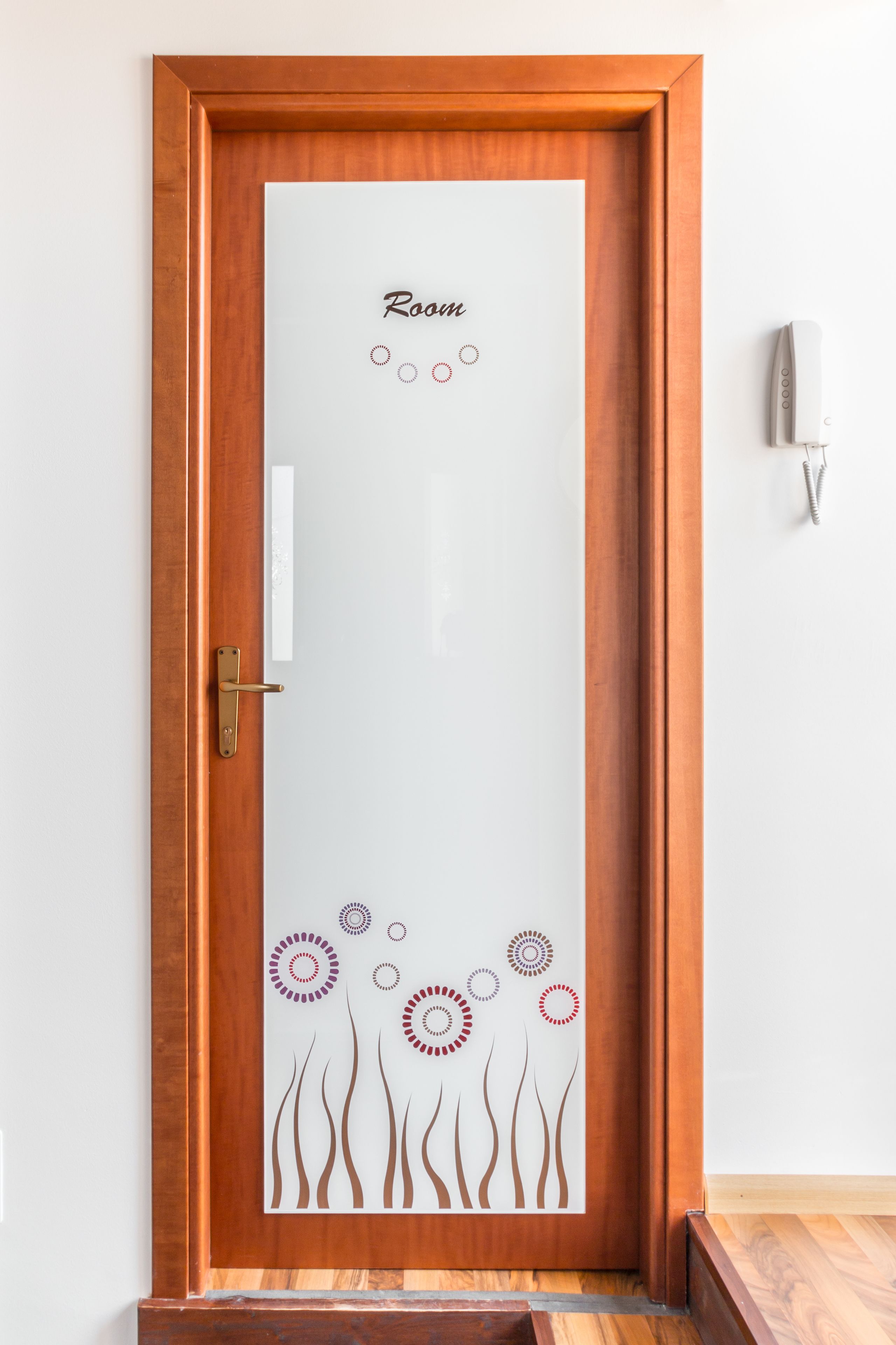 A wooden door with a frosted glass panel, a brass handle, and a decorative floral design.
