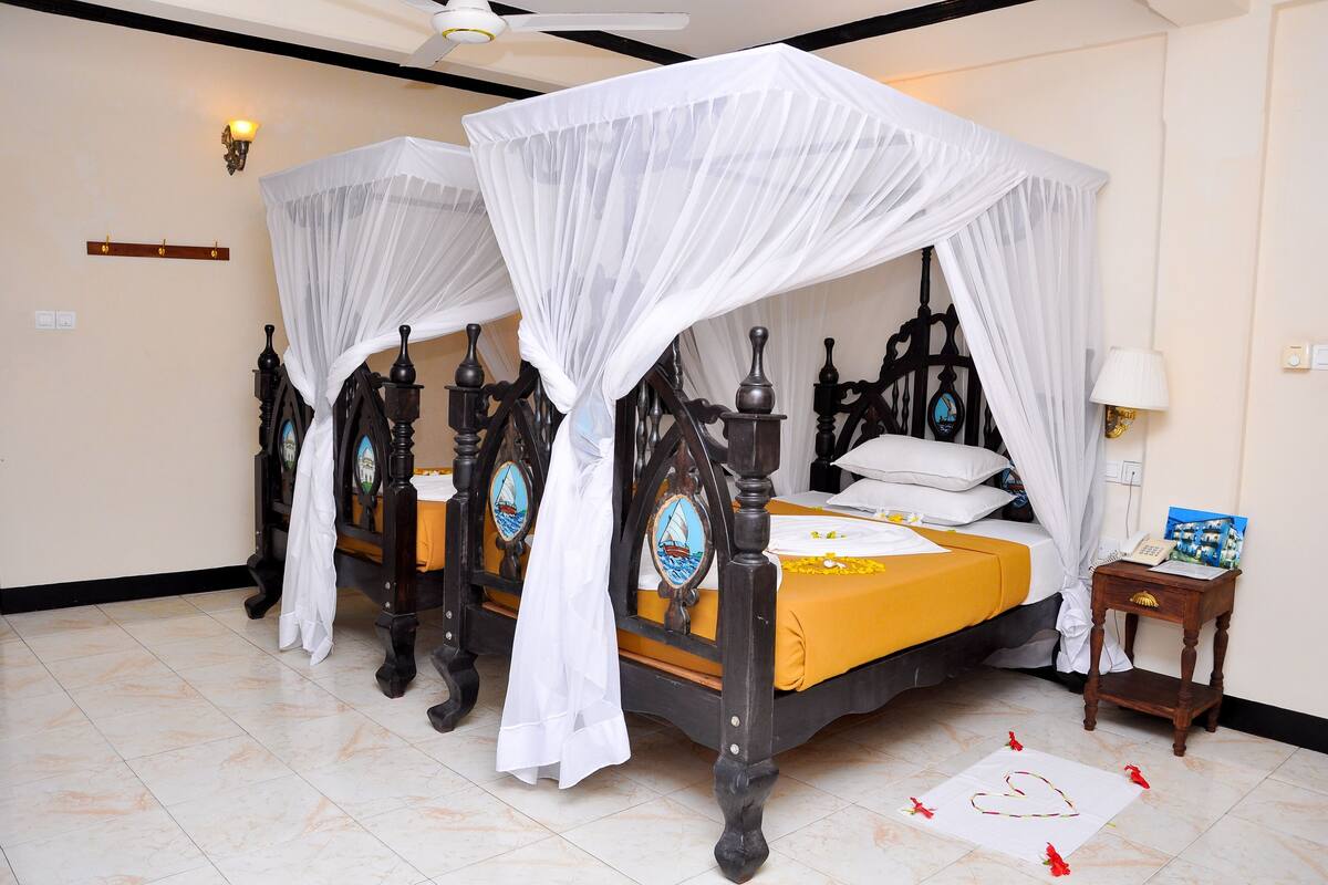 A four-poster bed with white canopy, a bedside table with a lamp, and a bedspread with a yellow border.