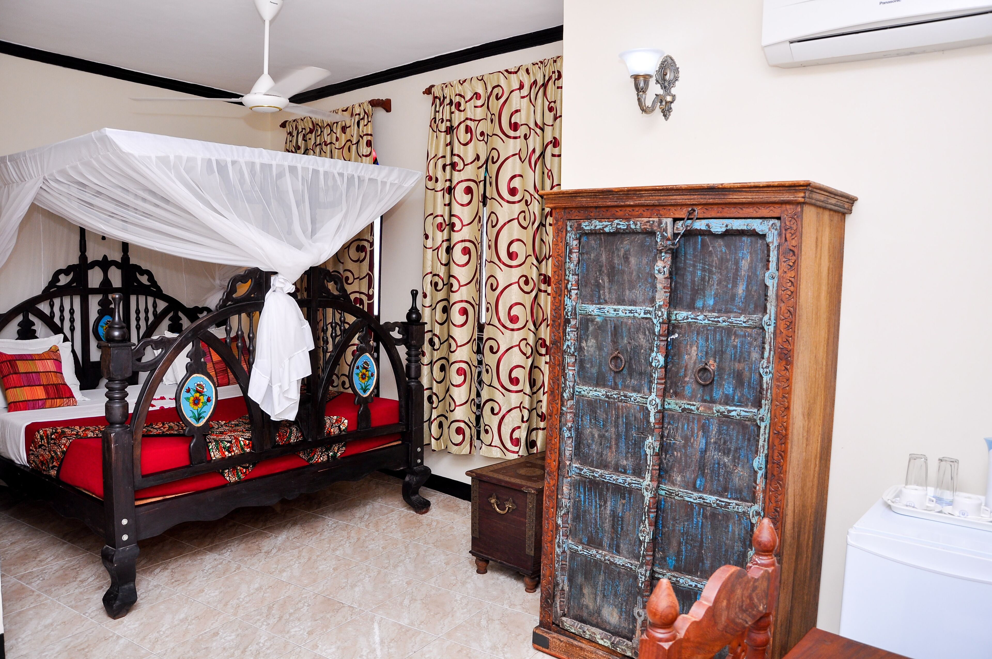 Un dormitorio con cama con dosel, un aparador de madera y cortinas estampadas.