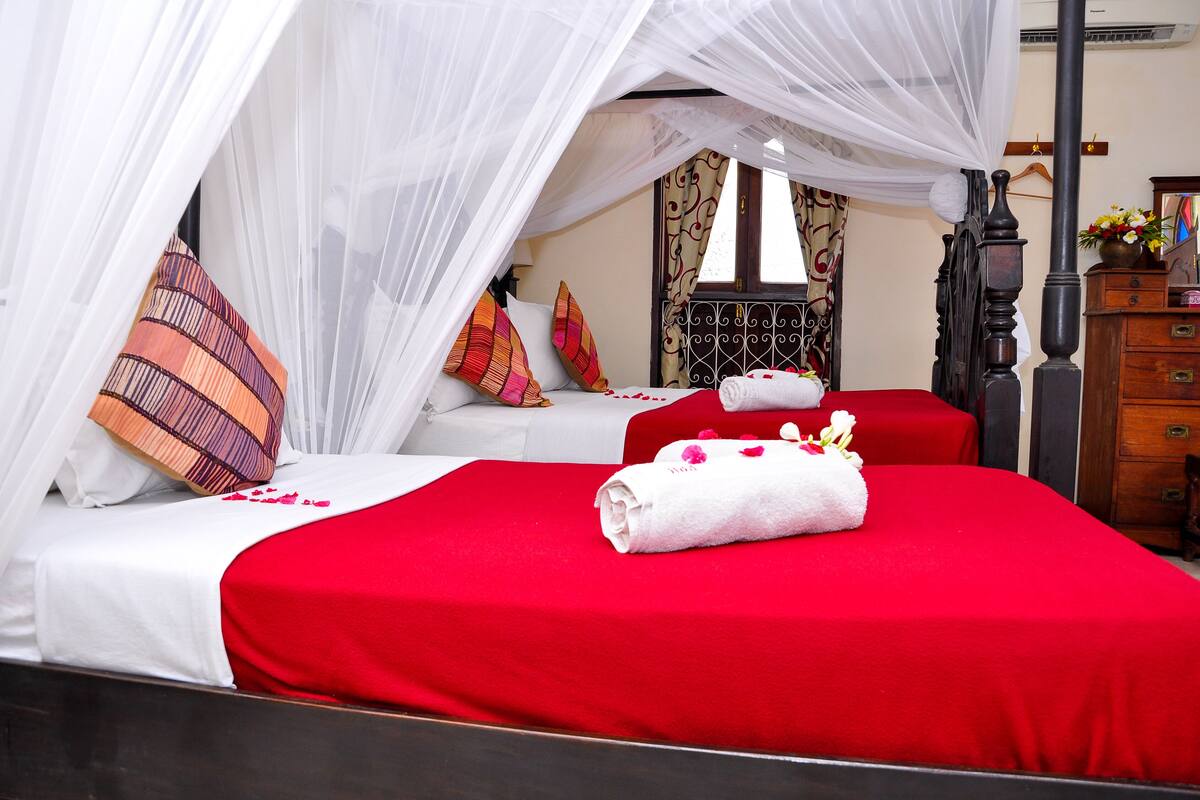 A hotel room with a canopy bed, a separate bed, and a wooden dresser.