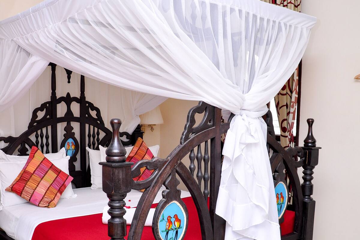 A four-poster bed with a canopy, red bedding, and colorful pillows.