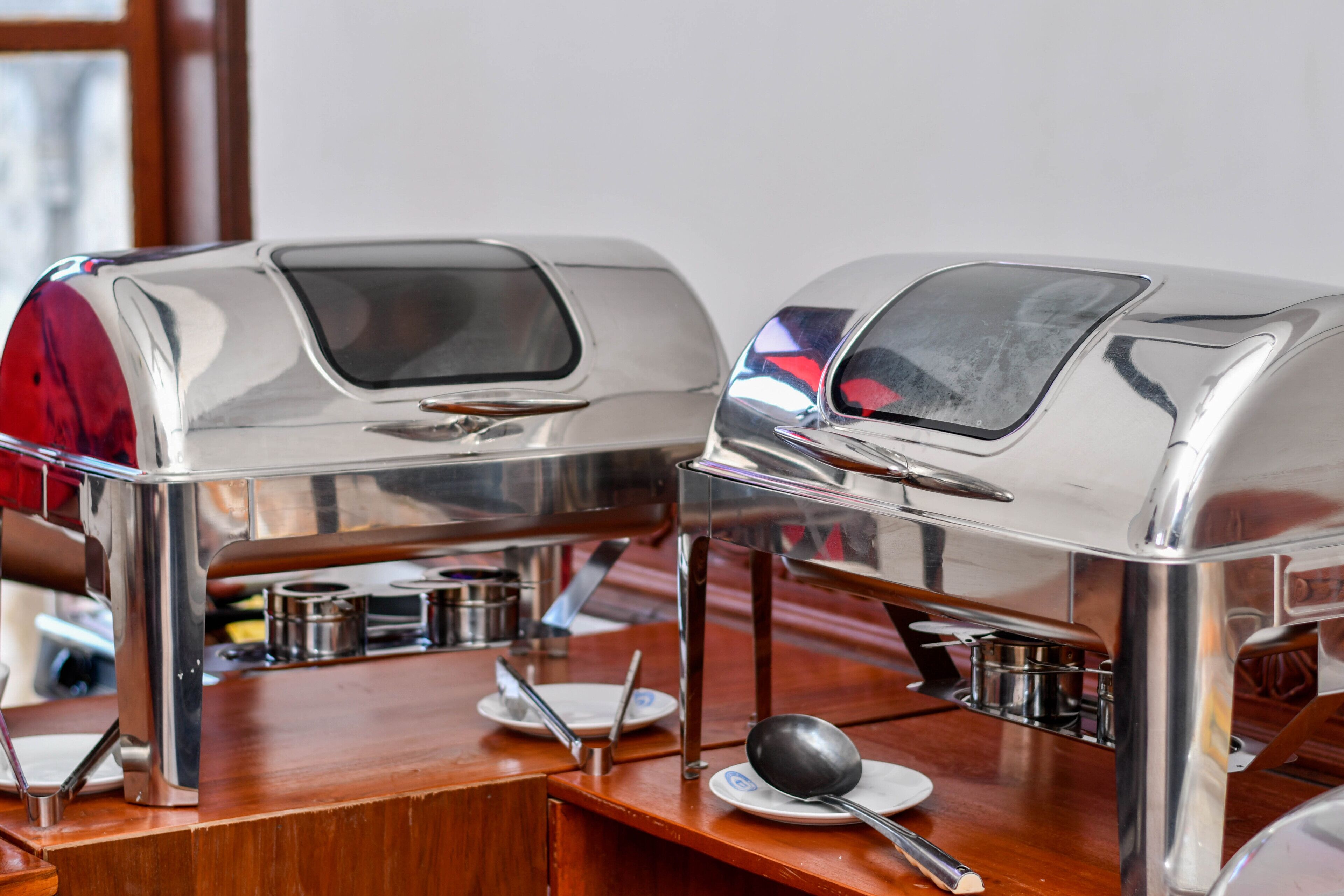 A buffet setup with two stainless steel appliances, a wooden table, and various serving utensils.