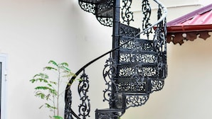 A spiral staircase with ornate black railings, a potted plant, and a wooden chair. - Forodhani Park Hotel (Zanzibar Town)