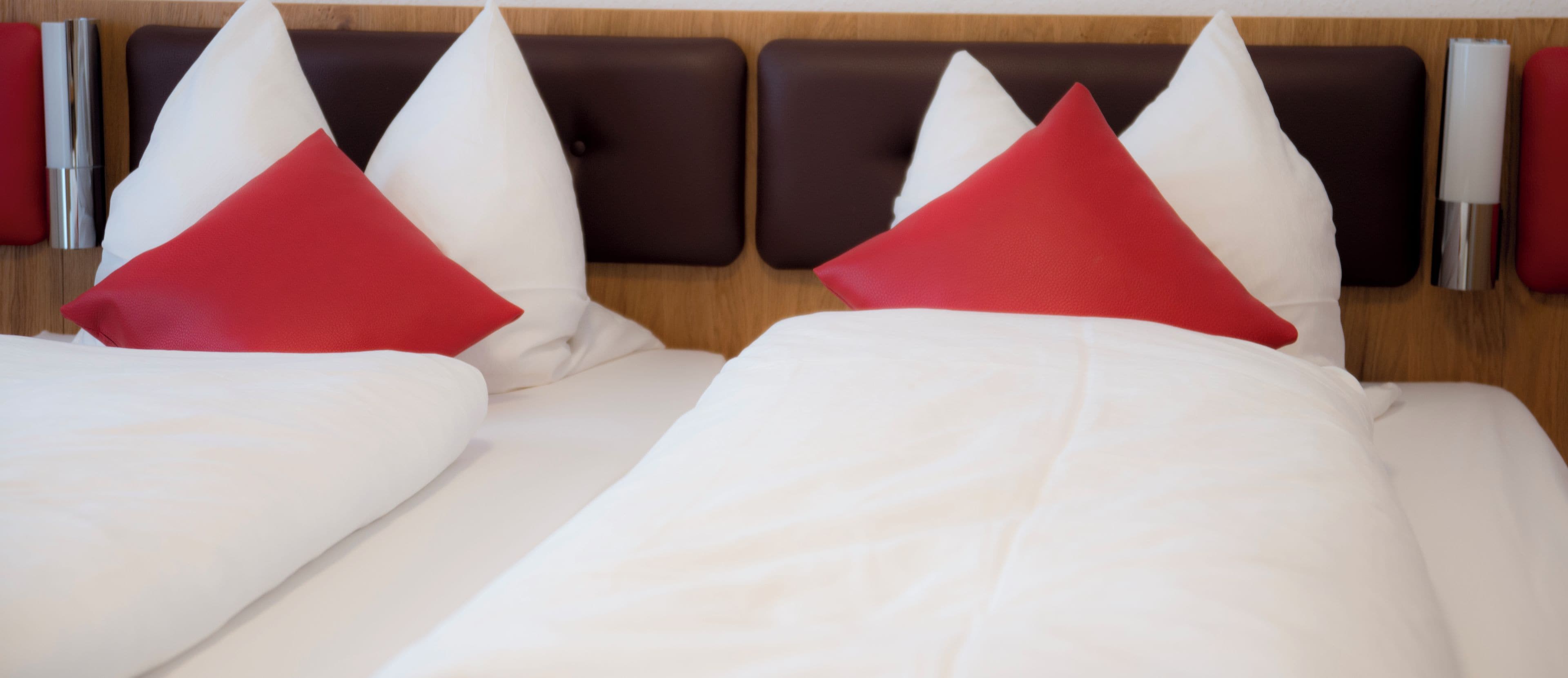 A hotel room with two beds, each with white bedding and red pillows.
