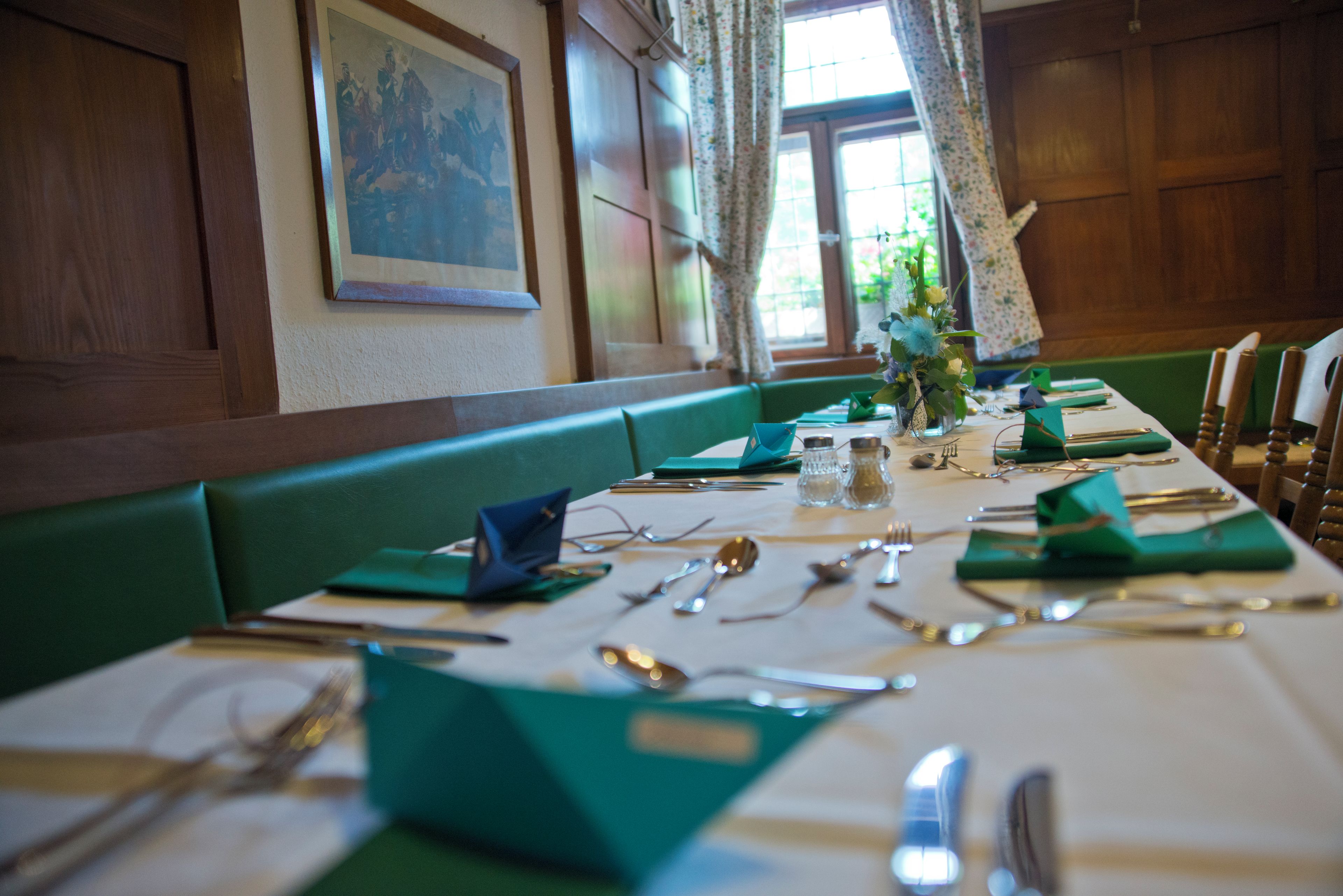 Une table à manger dressée avec des serviettes vertes, des couverts en argent et un vase rempli de fleurs.