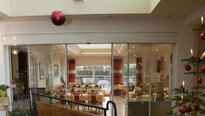 Un hall d’hôtel moderne avec un plafond haut, une cloison en verre et un sapin de Noël décoré.
