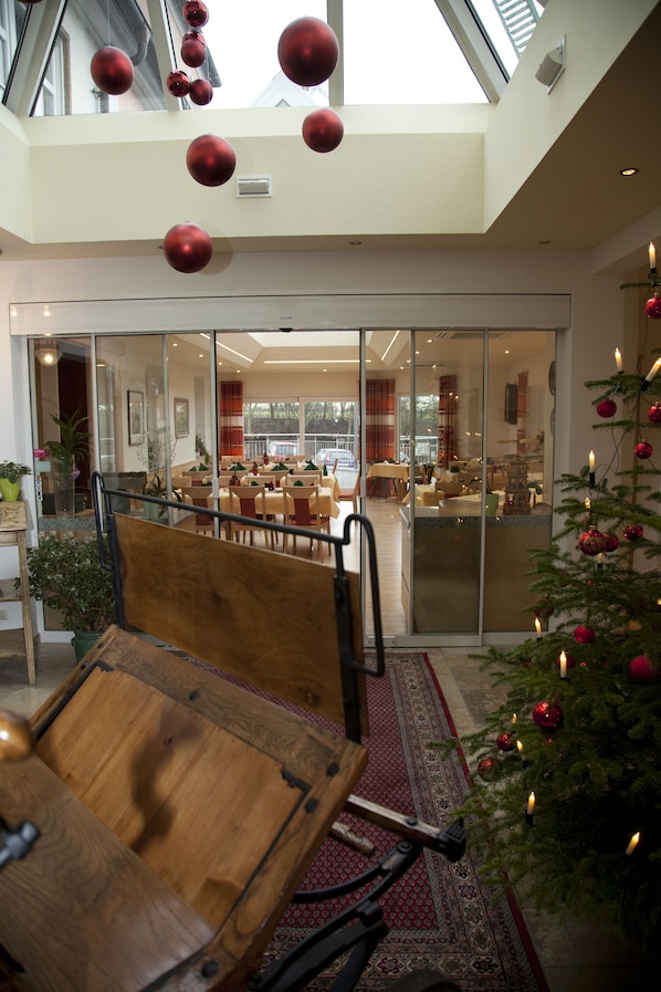 Un hall d’hôtel moderne avec un plafond haut, une cloison en verre et un sapin de Noël décoré.