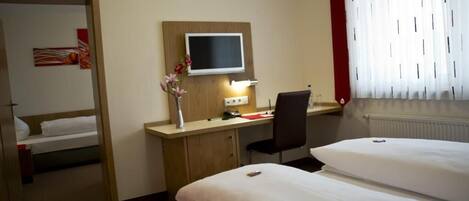 Habitación de hotel con dos camas, un escritorio con silla, televisor y un jarrón con flores.